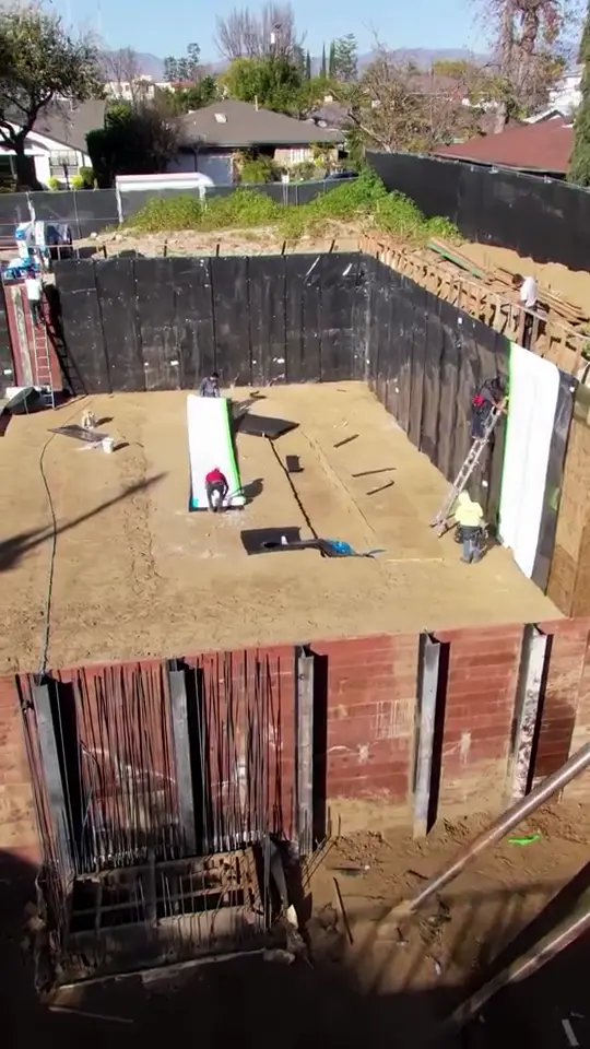 Shored excavation — Blindside waterproofing on a shored below-grade wall, crew at work.